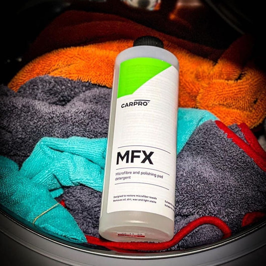 Una botella de detergente de microfibra Carrlo MFX colocada sobre una pila de toallas coloridas en una lavadora.