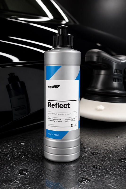 Botella de CarPro Reflect sobre una superficie reflectante, con piezas de automóvil al fondo.