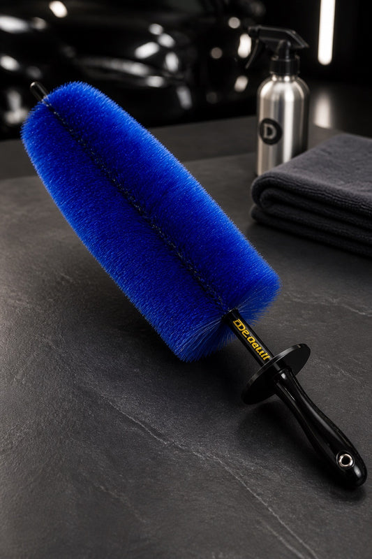 Cepillo azul para limpiar coches con mango negro sobre una superficie oscura, con un coche y productos de limpieza al fondo.

Detalles